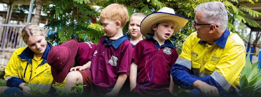 Stanwell staff members in high vis interact with young school children in uniform in a garden