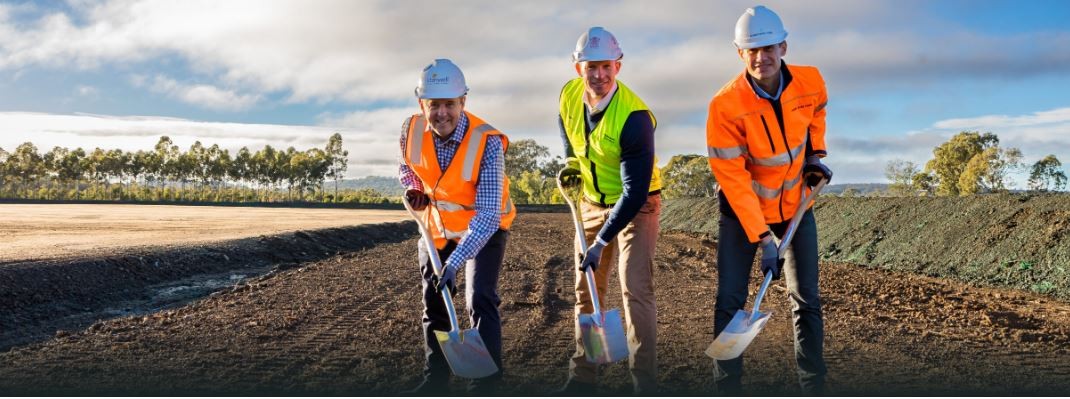 Three men in high vis and hard hats pose with shovels