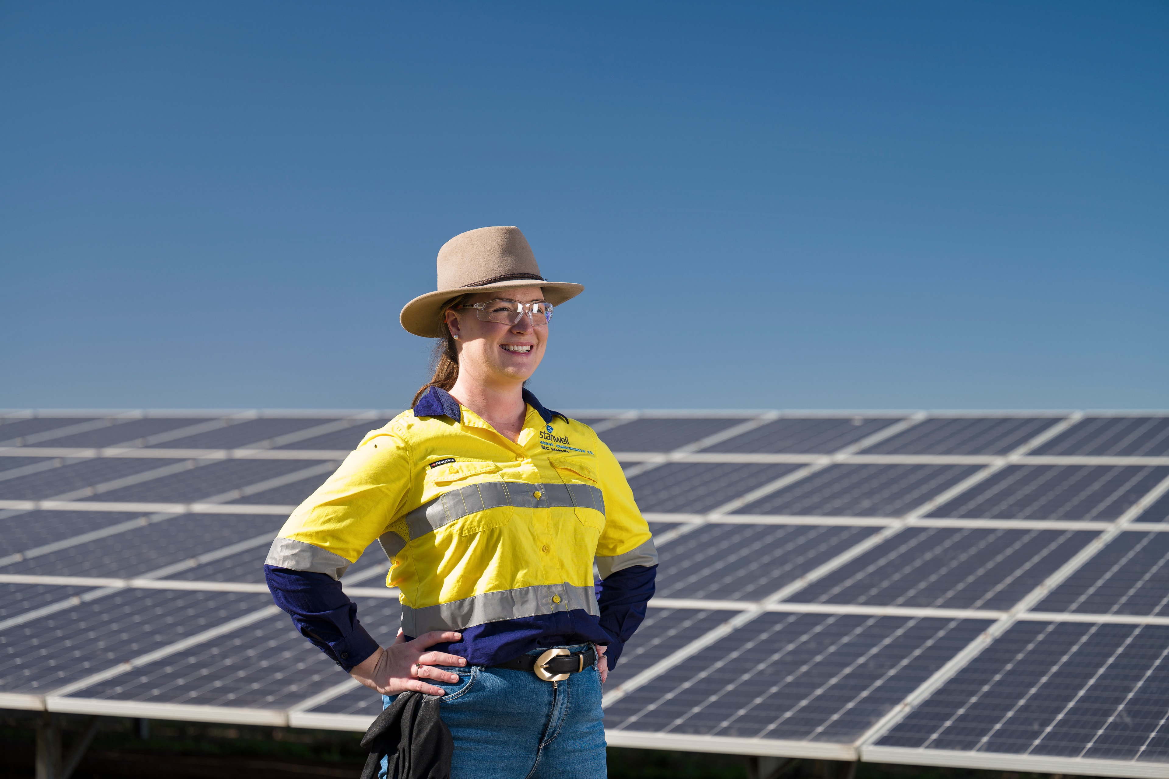 Bec Manley in hi vis, smiling with her hands on her hips in front of solar panels